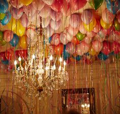 a chandelier is surrounded by balloons and streamers hanging from the ceiling in a room