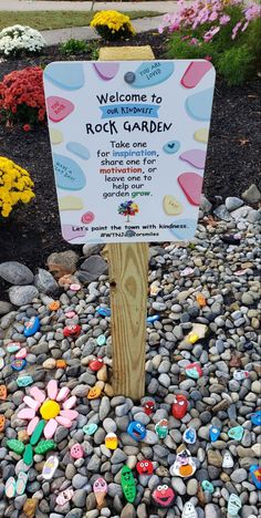 a rock garden sign in the middle of some rocks and gravel with flowers around it