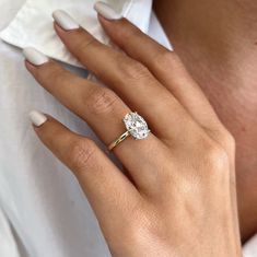 a woman's hand with a diamond ring on her left hand, wearing a white shirt