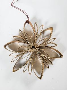 a gold ornament hanging from a string on a white surface with a brown cord