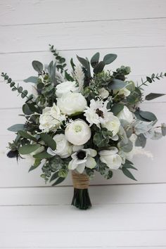 a bridal bouquet with white flowers and greenery on a wooden stand against a white painted wall