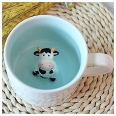 a small toy cow sitting in a coffee cup filled with water on top of a woven place mat