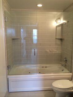 a white toilet sitting next to a bath tub in a bathroom under a light fixture