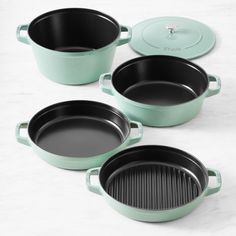 four green cast iron pots with lids on a white countertop next to a frying pan