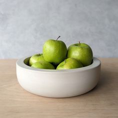 a white bowl filled with green apples on top of a wooden table