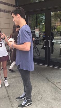 a man is standing on the sidewalk and looking at his cell phone while people are walking by