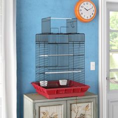 a bird cage sitting on top of a dresser next to a wall with a clock