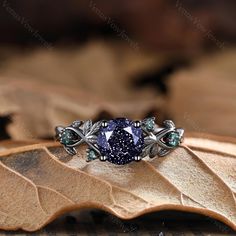 a fancy ring with blue and green stones on top of leafy brown leaves in the background