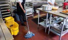 two people in a kitchen cleaning the floor with a mop and dustpans