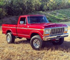 a red pickup truck parked on top of a dry grass field next to a forest