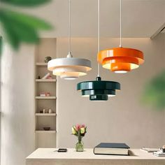 three lights hanging from the ceiling above a table with books and flowers in vases