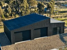 an aerial view of a black building in the middle of a field with trees and grass