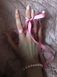 a person's hand with a pink ribbon tied around it on top of a bed