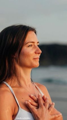 a woman standing on the beach holding her chest