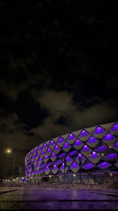 the building is lit up with purple lights in front of dark clouds and blue sky