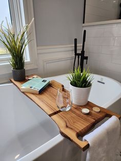 a bath tub with a wooden tray and two plants on the edge next to it