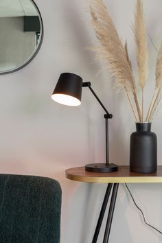 a black lamp sitting on top of a wooden table next to a mirror and chair