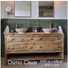 a bathroom with two sinks and mirrors on the wall next to a wooden dresser in front of green tiled walls