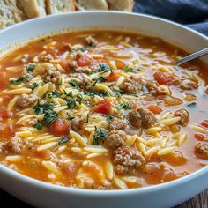 a white bowl filled with pasta and meat soup next to some bread on the side