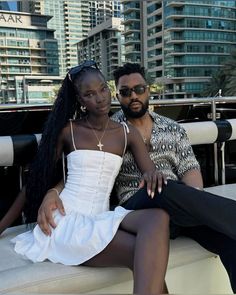 a man and woman sitting next to each other on a boat in front of tall buildings