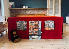 a teddy bear sitting in front of a red cloth covered table with pictures on it