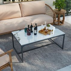 a table with bottles and glasses on it sitting in front of a couch, next to a potted plant