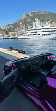 a purple sports car parked in front of a large white boat on the water next to a dock