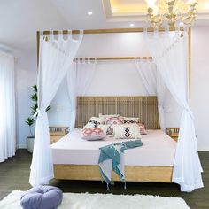 a bed with white drapes and pillows on top of it, next to a chandelier