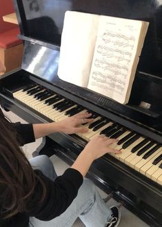 a woman sitting at a piano playing an old book on it's organ keyboard