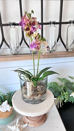 a glass vase filled with flowers sitting on top of a white table next to other plants