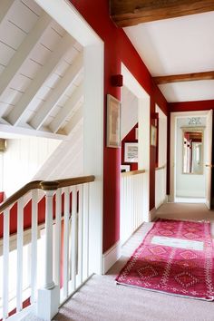 a hallway with red walls and white railings, carpeted flooring and rug on the ground