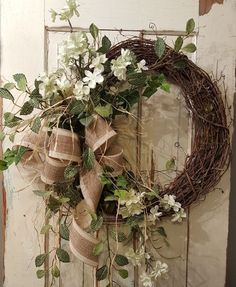 a wreath with white flowers and green leaves hanging on a door handle, decorated with burlap