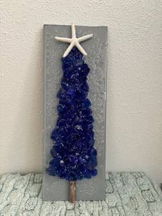 a blue glass christmas tree with starfish on the top and sea shells in the bottom