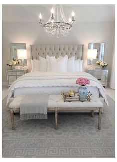 a bedroom with a large white bed, chandelier and two tables in front of it