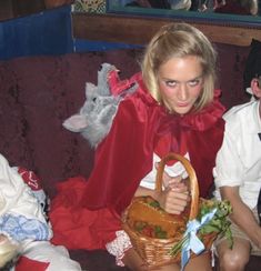 two people sitting on a couch with one holding a basket and the other wearing a red cape