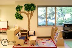 a child's playroom with toys and trees on the wall, in front of a large window