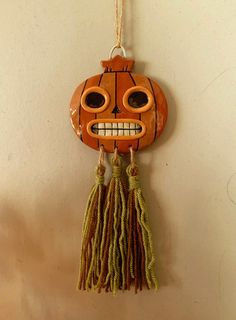 an orange pumpkin hanging on a wall with tassels around it's eyes