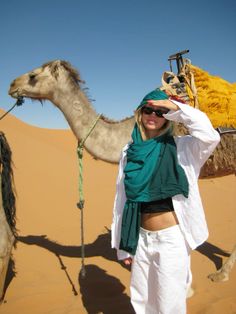 a woman standing in the desert next to a camel