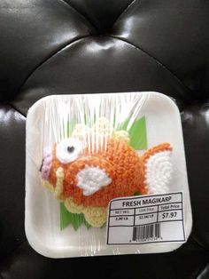 a plastic tray with a crocheted orange fish on it's side and the label says fresh magkap