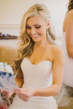 a woman in a wedding dress is looking at something on her tabletop and smiling