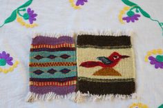 two small rugs on a table with flowers and leaves in the background, one has a bird