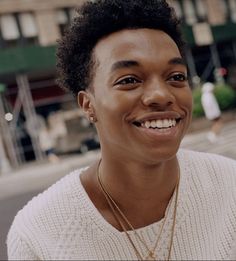 a woman with short hair smiling and wearing a white sweater on the street in front of a building