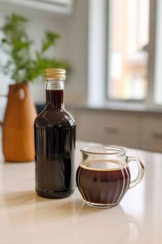 a bottle of liquid sitting on top of a table next to a glass cup filled with liquid