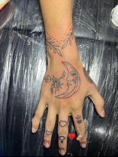 a person's hand with tattoos on it and the moon in the sky above them