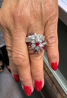 a woman's hand with red and white nail polish holding an engagement ring