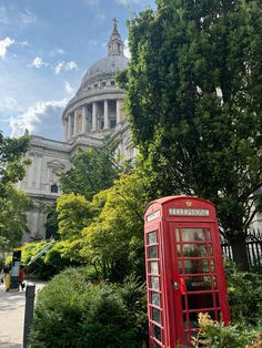 a red phone booth sitting in front of a tall building with a dome on top