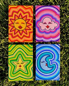 four square paintings on grass with sun, moon and cloud in the middle one has a smiley face