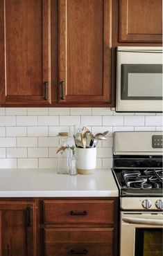 a kitchen with wooden cabinets and white counter tops, silver stove top oven and microwave