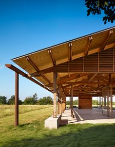 an outdoor covered area with benches and tables on the grass, under a blue sky