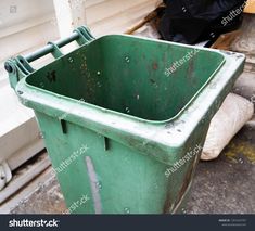 a green trash can sitting next to a building